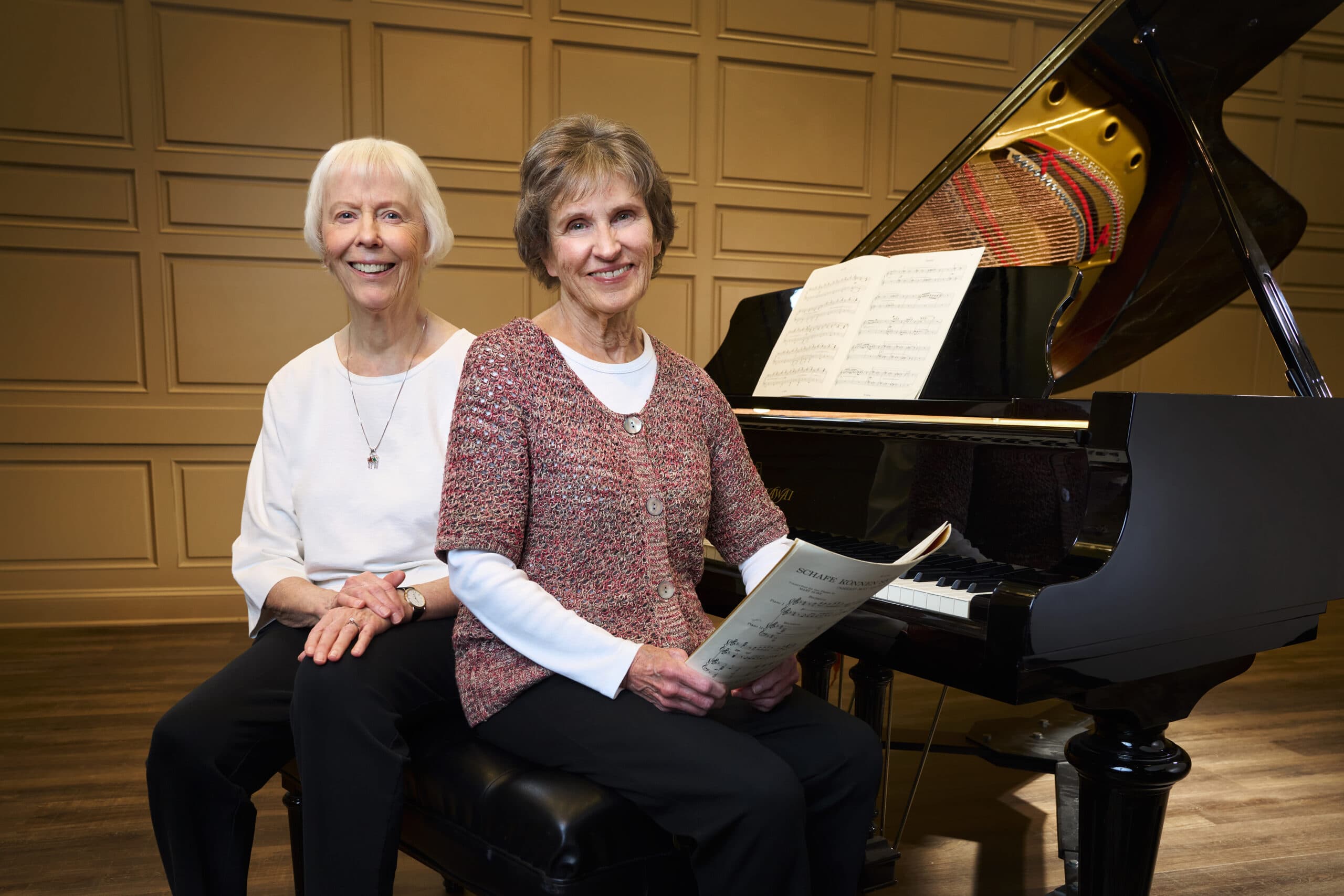 Two pianists sit on the bench of a baby grand piano.