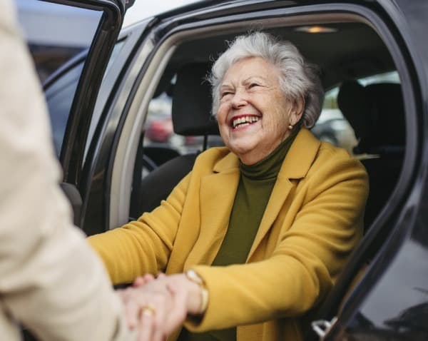 Older woman in a yellow jacket getting out of a car.